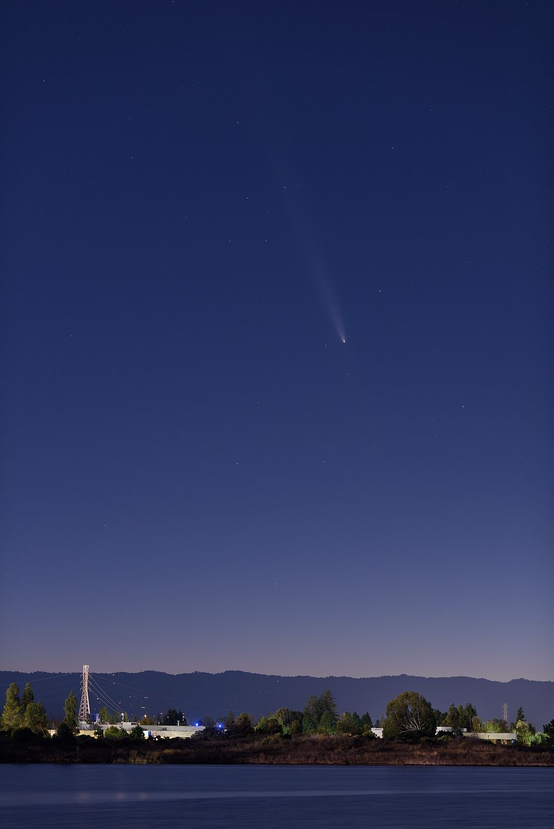 Comet C/2023 A3 with a long tail over a twilight shoreline